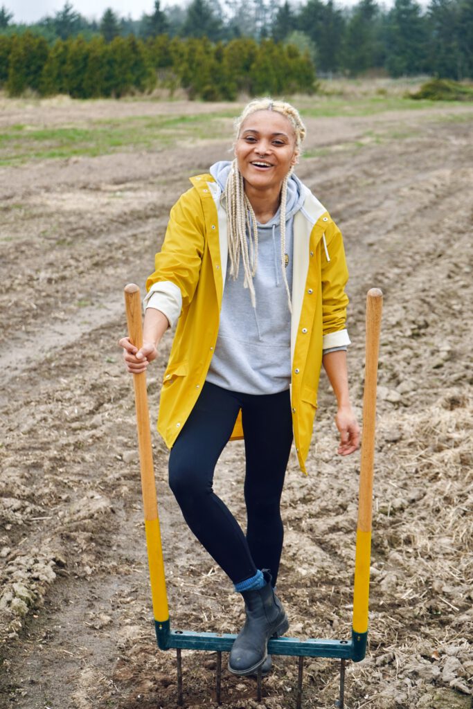 Nicole Portrait Smiling Black fem farmer loosening soil with a broadfoark