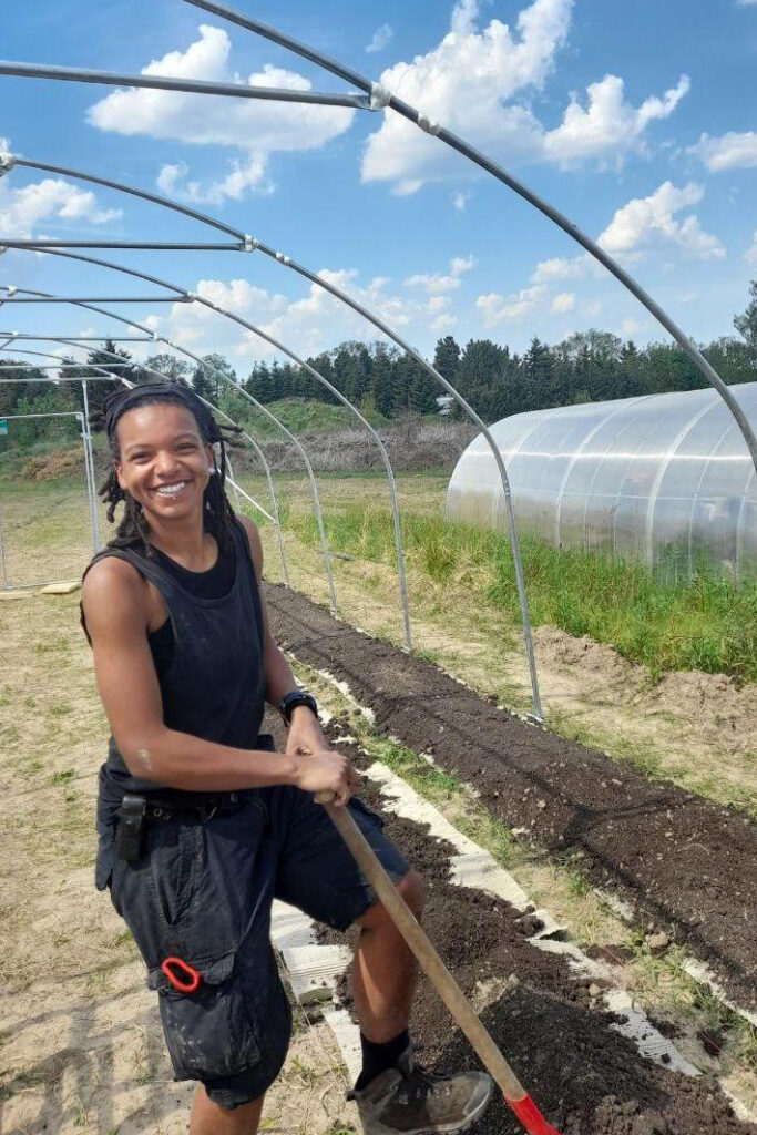 Smiling Black fem farmer raking a market garden bed - 2.3